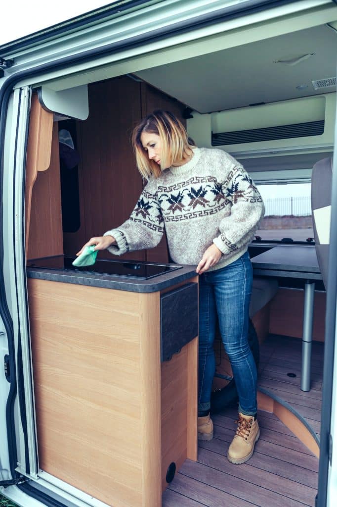 Woman cleaning kitchen of a camper van with a cloth